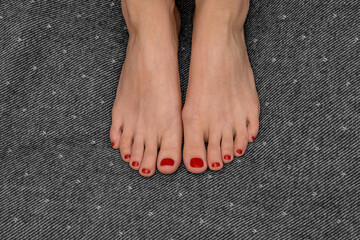 When passion passes through the foot. Feet of a young girl with fiery red nail polish on gray and...
