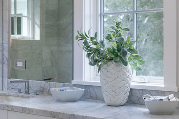 Interior of a modern bathroom with decorative white vase, marble counter and picture window near sink and mirror.