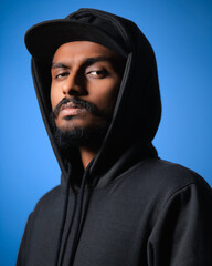 Young Indian man wear black hoody casual clothes look camera with intense isolated on plain blue...