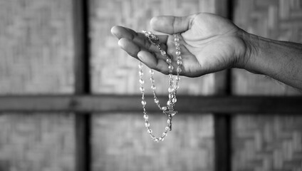 Person holding a rosary in hand in black and white background with light. Praying rosary concept,...
