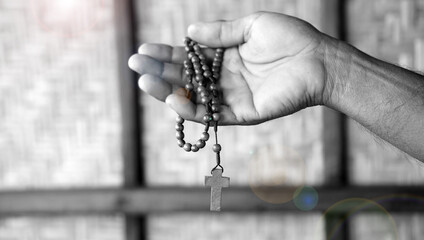 Person holding a wooden rosary in hand in black and white background with light. Praying rosary...