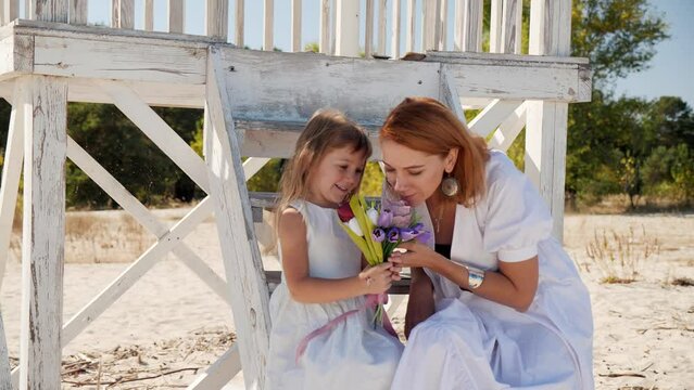 Mom and daughter in white dresses spend time together on the beach and have fun