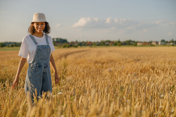 Naklejka na ściany i meble Smiling woman agronomist standing in a wheat field and checks the harvest. High quality photo
