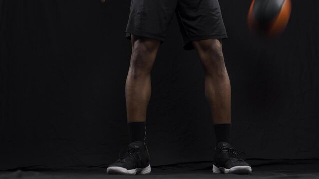 Basketball player bouncing a ball. African american sports man practicing against black background..