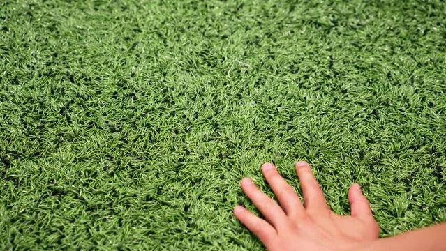close-up of a hand running across a football synthetic grass with a rubberized texture