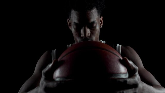 Basketball player sitting on a bench taking deep breath in. Concentrated african american sports man against black background.