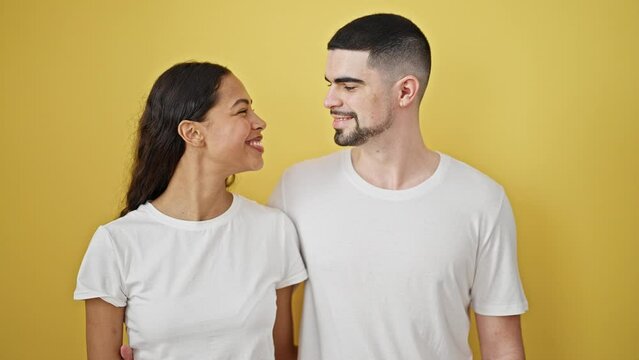 Beautiful couple standing together, conveying confidence and love through a sweet kiss against an isolated yellow background