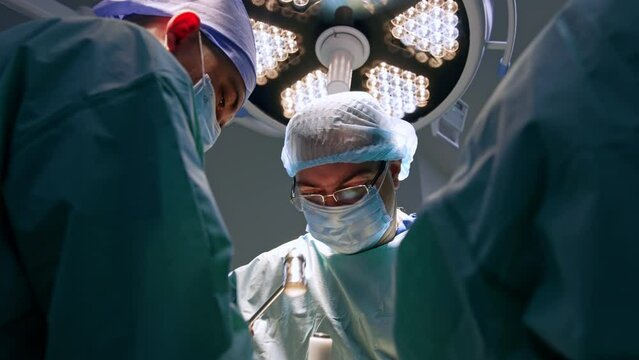 Professional male surgeon in glasses uses mallet and chisel at foot operation. Medical team working in surgery room. Low angle view.