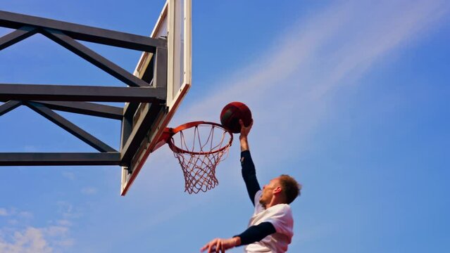 Tall guy basketball player jumps to the hoop with the ball in his hand to score a spectacular dunk during practice on the basketball court in the park