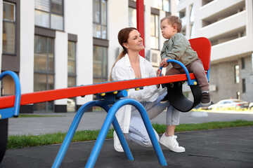 Happy nanny and cute little boy on seesaw outdoors