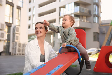 Happy nanny and cute little boy on seesaw outdoors
