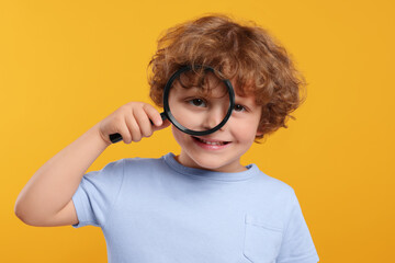 Cute little boy looking through magnifier glass on orange background