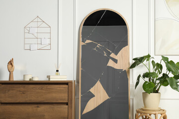 Broken mirror, wooden chest of drawers and houseplant in room