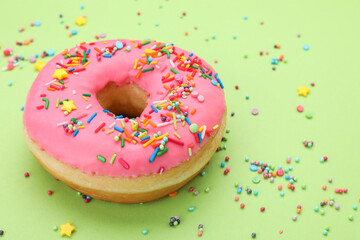 Glazed donut decorated with sprinkles on green background, closeup. Space for text. Tasty...
