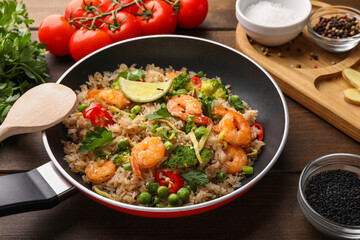 Tasty rice with shrimps and vegetables in frying pan on wooden table, closeup