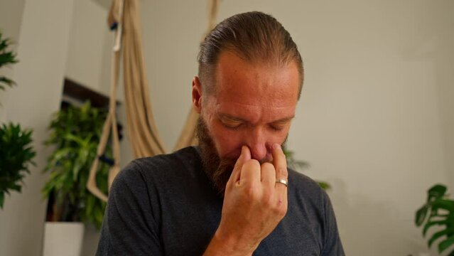 a yogi man with a beard performs breathing practices through the nose during meditation in the hall to improve well-being