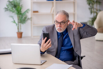 Naklejka premium Old male employee talking by phone at workplace