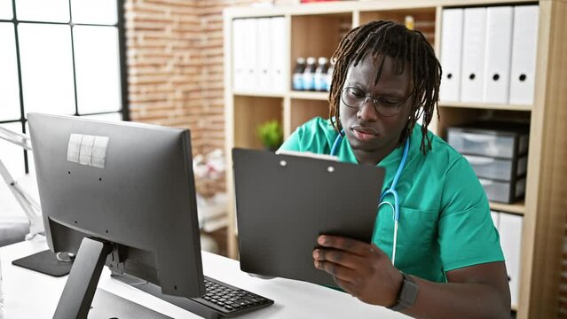 African american man doctor using computer taking notes at the clinic