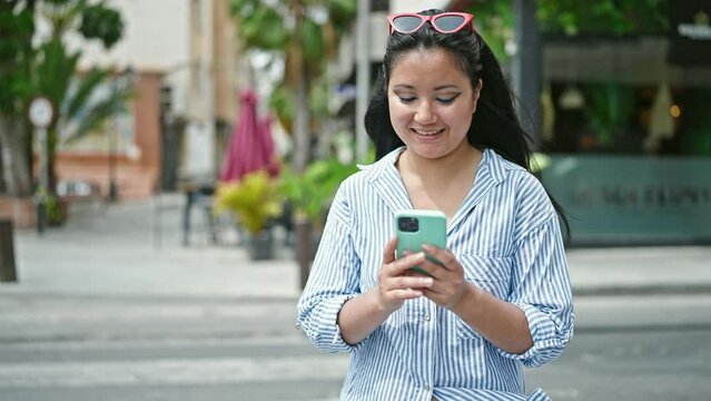 Young chinese woman using smartphone smiling at coffee shop terrace