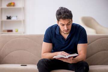 Young male student reading book at home