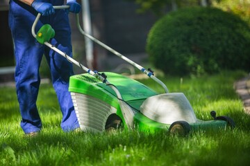 Professional garden worker, working with electric lawn mower on grass