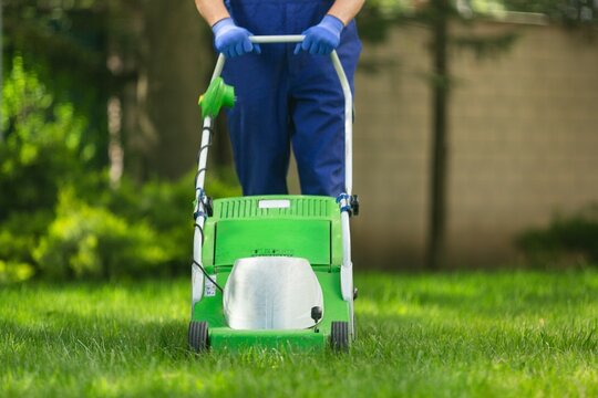 Professional garden worker, working with electric lawn mower on grass