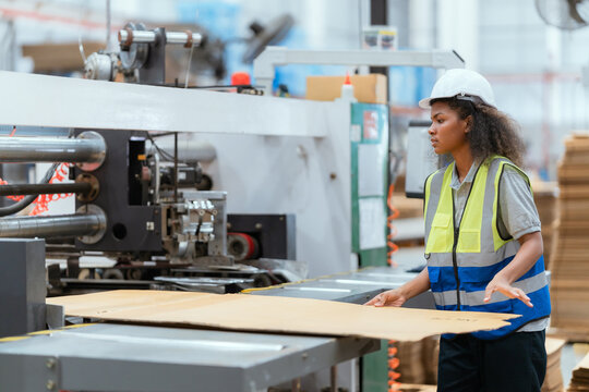 A female employee is using a machine to sew cardboard boxes in a warehouse.