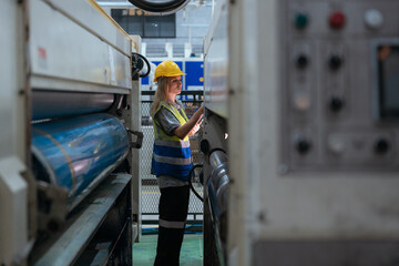 Male and female technicians are inspecting a large paper production machine.