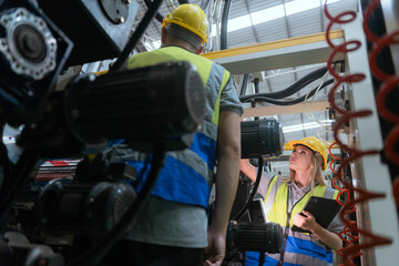 Male and female technicians are inspecting a large paper production machine.
