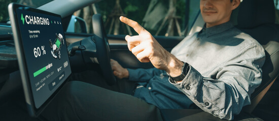 Electric car driver checks battery charging status, range and charging limit on app screen in the car. Smart technology device show EV car recharging data of electric storage in car battery innards.