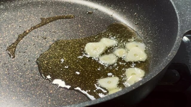 ニンニクをオリーブオイルを使ってテフロンのフライパンで炒めているシーン