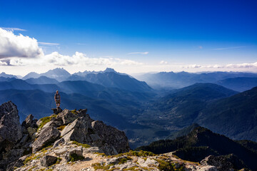 Adventurous athletic male hiker standing on top of a rugged mountain in the Pacific Northwest with jagged mountains in the background.
