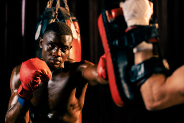 Fototapeta na wymiar African American Black boxer punching at trainer or coach wearing punching mitts as boxing bag training equipment in the gym. Strength and stamina training for professional boxing match. Impetus