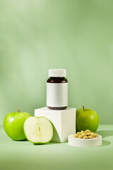 Medicine bottle standing on white podium with green apple surrounded. Some pills are arranged. Medicine, treatments and healthcare with Green Apple (Malus domestica) extract