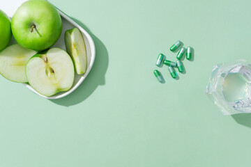 Against the green background, dishes of green apples with capsule pills and glass cup decorated....