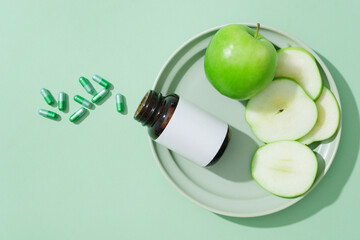 Ceramic dish featured several slices of green apple and a medicine bottle. Green capsules placed on...