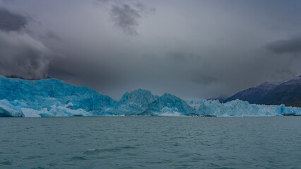 The amazing Perito Moreno glacier. A wall of blue ice over a turquoise glacial lake. Ripples on the water. Mountains in the fog. Clouds in the sky. Argentina. El Calafate. Los Glaciares National Park.