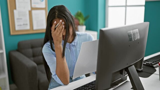 Young latin woman business worker using computer reading document looking upset at the office