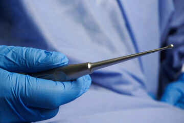 Doctor wearing blue medical gloves holding bone curette.