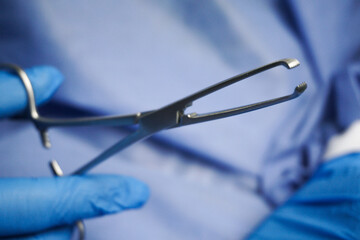 Doctor wearing blue medical gloves holding Allis Intestinal and Tissue grasping forceps, are serrated surgical forceps used for ligation and clamping of bleeding in uterus during surgery