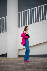 a glamorous girl in a bright colored jacket walks down the street with her jacket pulled down and wearing jeans