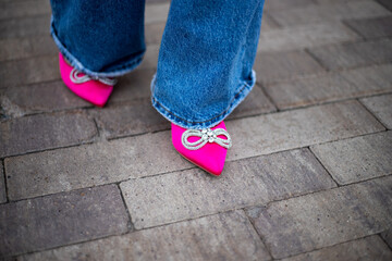 close-up of a woman's legs in jeans with bright fuchsia high-heeled shoes on the street