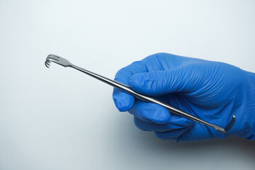 Doctor wearing blue gloves holding sharp Senn-Miller Retractor is a multi-purpose, dual-ended...