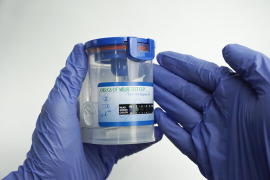 Hand in blue glove holding an empty container for analysis. Drug test concept. Isolated on white background.