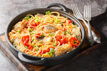 Main course spaghetti with white fish fillet, peppers, onions, green peas and tomato sauce close-up in a frying pan on the table. Horizontal