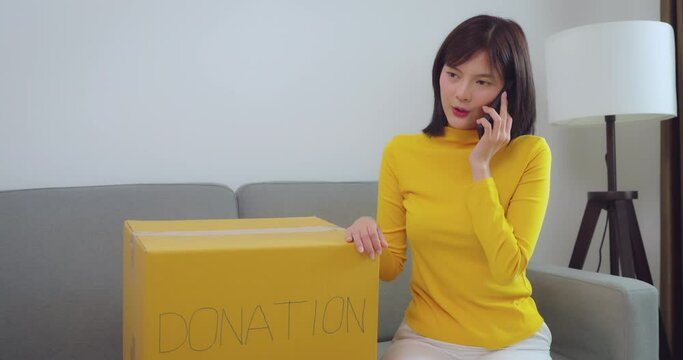 Asian woman using cell phone to donate clothes at home. She is in talks with a charity to donate clothes. Donation and Volunteer concept.