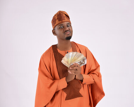 angry stingy upset rich African man wearing Yoruba Nigerian native traditional attire agbada irritated surprised holding new naira