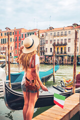 Fototapeta na wymiar Female tourist holding italian flag traveling in Italy- Venice city, canal and traditional gondola