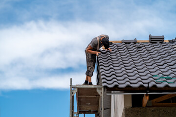 craftsman on scaffolding installs ceramic tile on the roof of a family home, copy space
