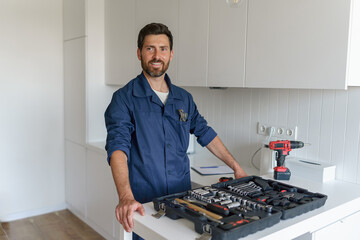 Smiling male worker with toolbox standing on home kitchen background and looking at camera